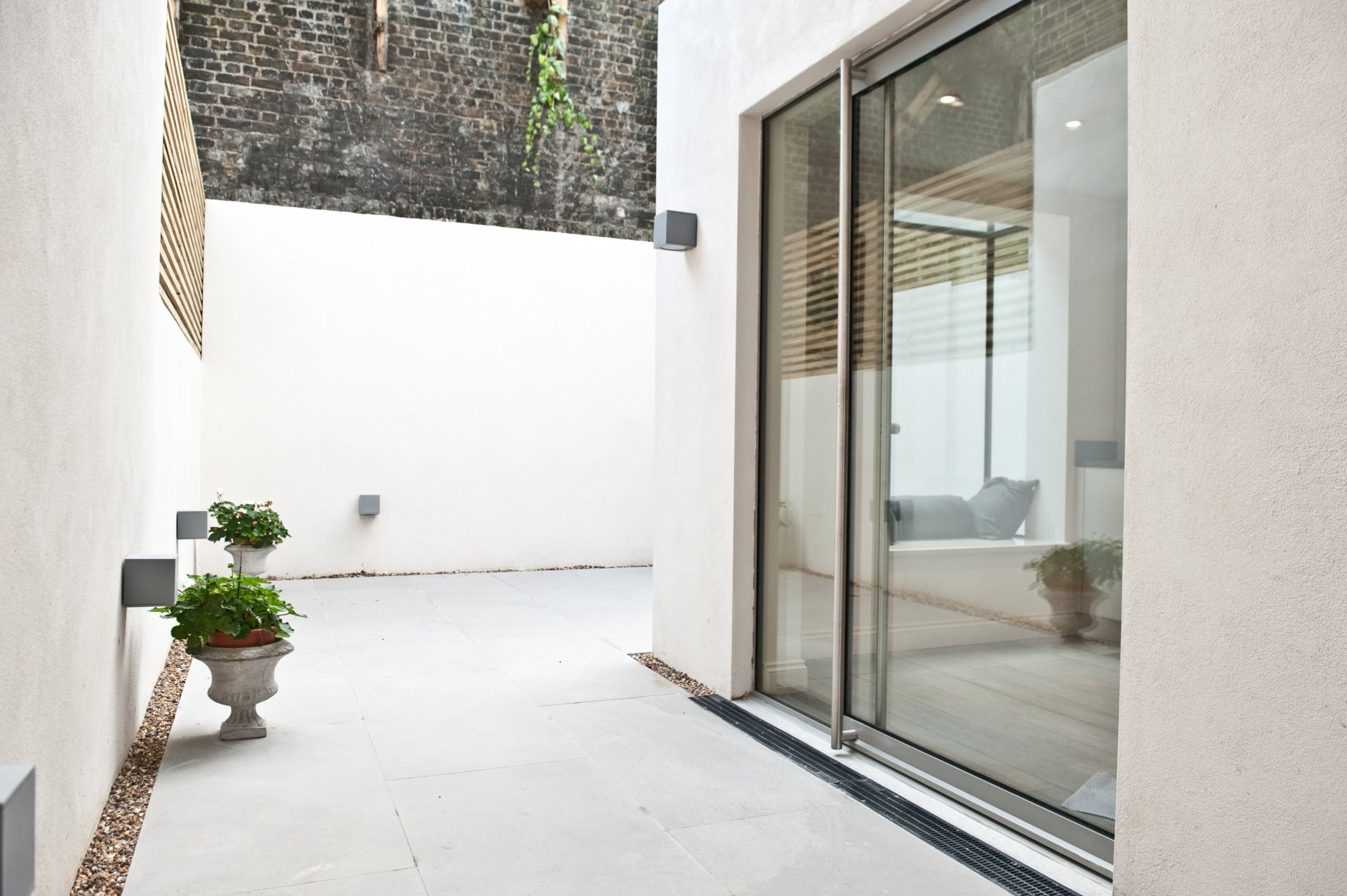 Rendered lightwell courtyard with stone paving, slim-frame sliding glass doors, linear drain and wall lights