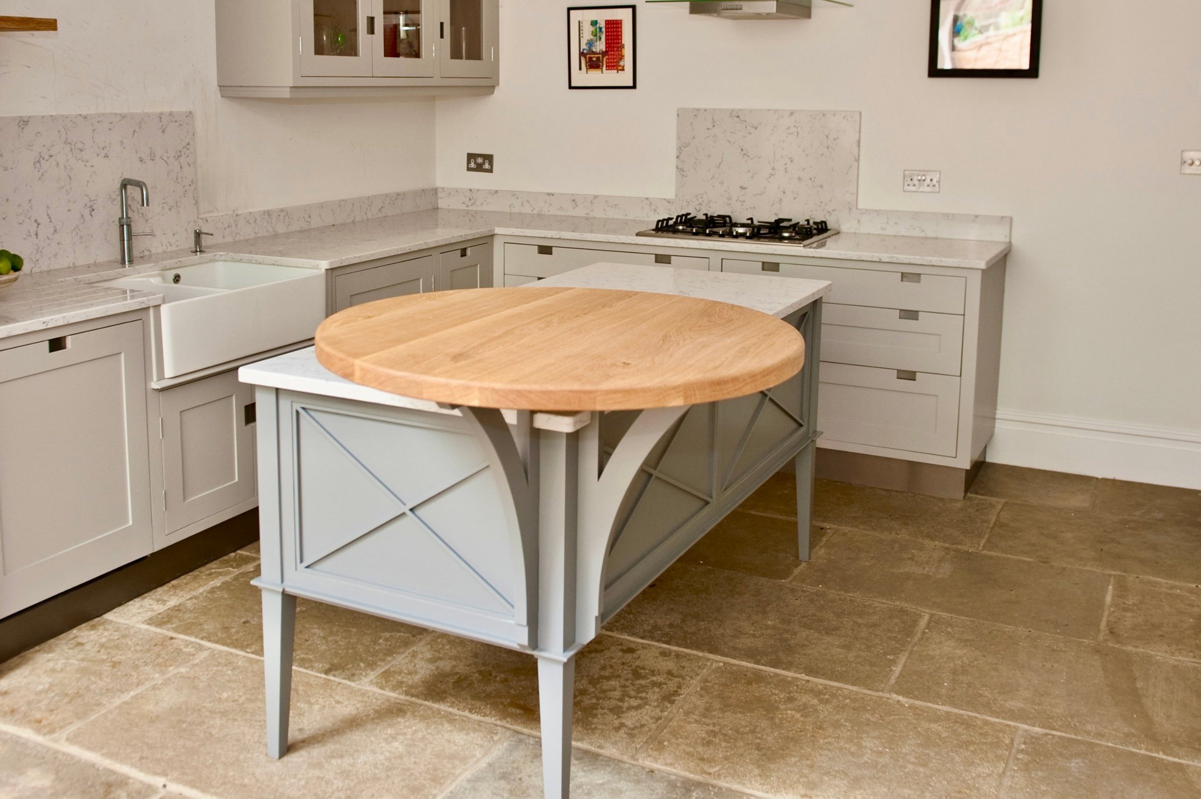 Bespoke hand-painted island with cross-braced panels, curved brackets, tapered legs and a round oak breakfast table, in a grey in-frame kitchen with a reclaimed limestone floor