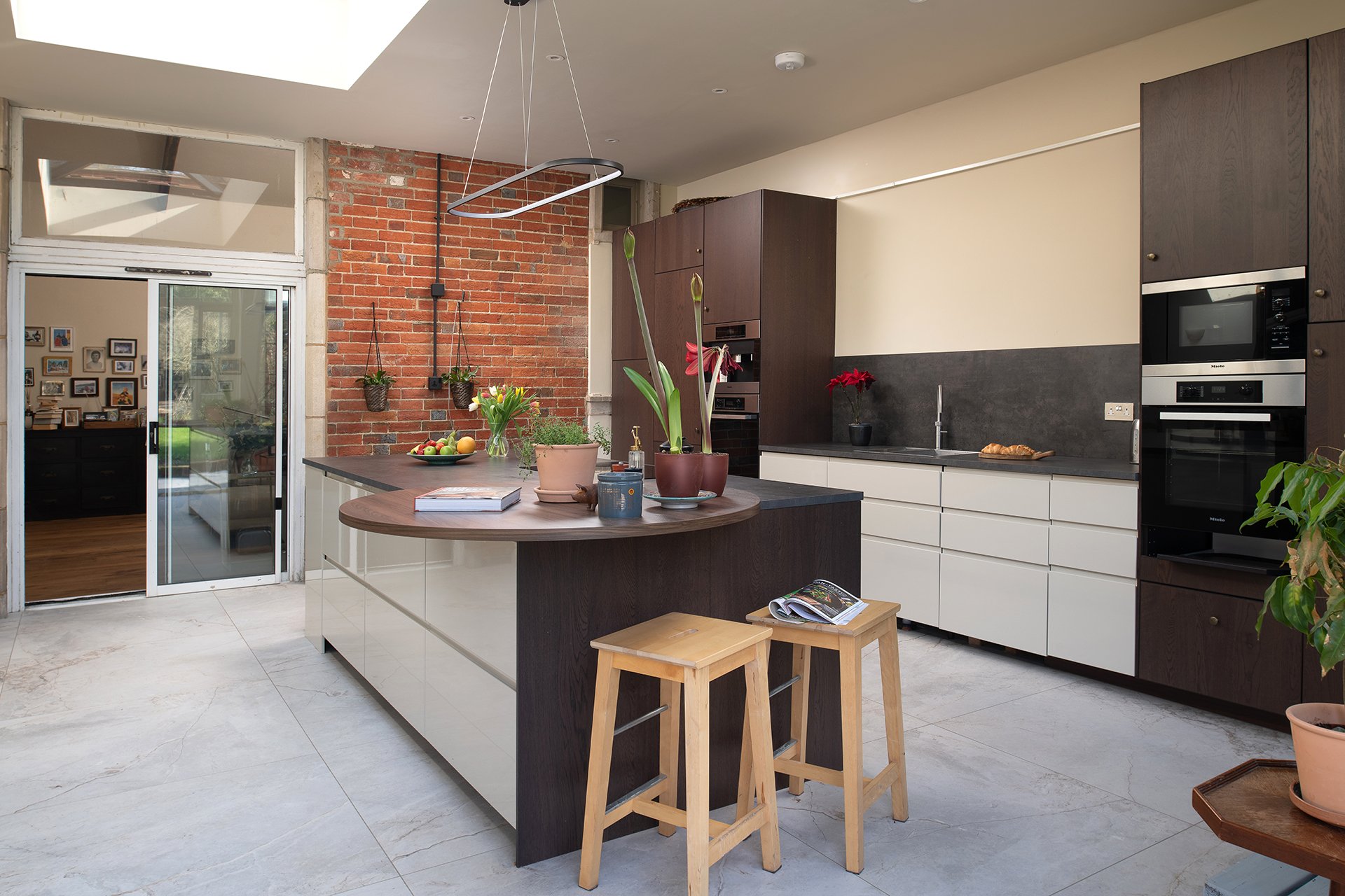 Kitchen extension with smoked oak and cream island, curved breakfast bar, exposed brick wall, rooflight, Miele ovens and large-format stone-effect floor tiles
